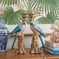 Decorative parrot statues on a wooden surface with a tropical-themed wallpaper in the background.